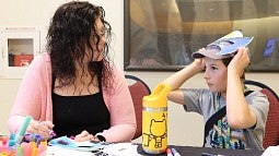 A woman smiles at a child who has a superhero mask on top of his head