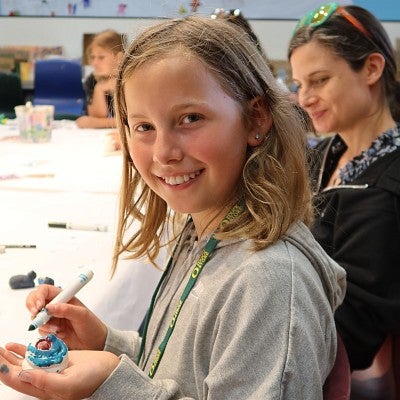 A child holds a clay animal sculpture while her mom smiles